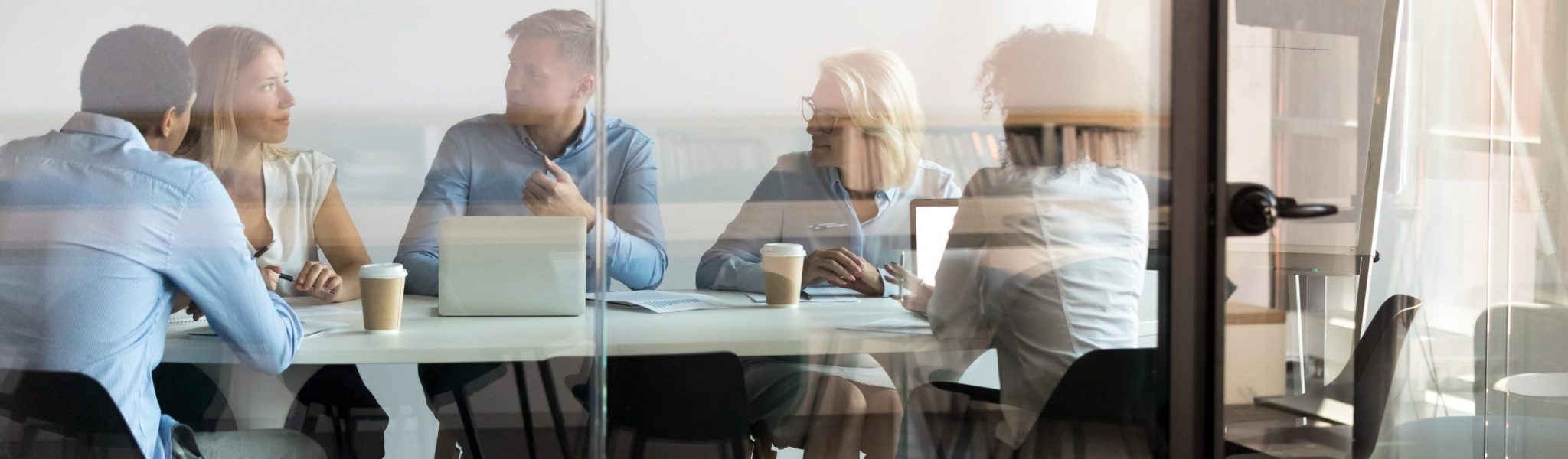 Advertising department brainstorming at modern office boardroom behind closed doors, view through the glass wall. Diverse staff led by ceo discussing new project sharing ideas thoughts and sales pitch