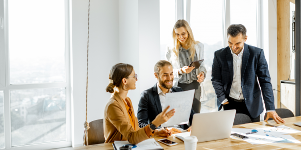 Groupofayoungofficeemployeesdressedcasuallyinthesuitshavingsomeofficeworkatthelargemeetingtableinthebrightsunnyroom.png